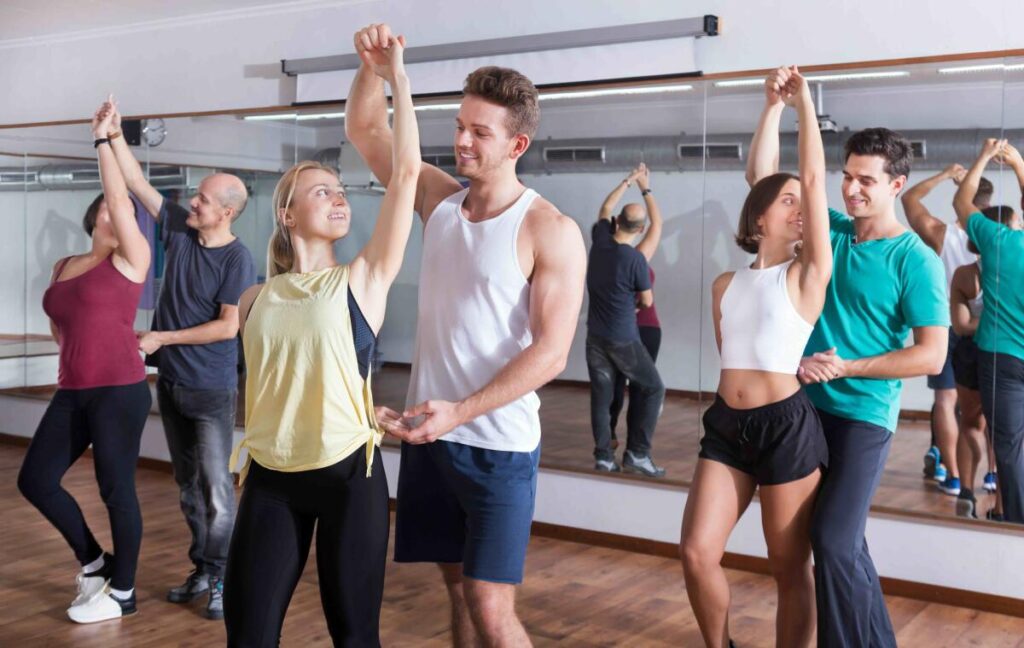 Grupa uśmiechniętych osób w różnym wieku tańczy energicznie w jasnej sali