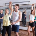 Grupa uśmiechniętych osób w różnym wieku tańczy energicznie w jasnej sali