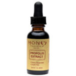 buteleczka propolisu w kroplach z kroplomierzem obok ula pszczelego na stole